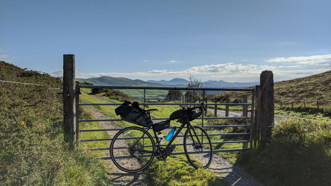 My bike with next to a fence near a hill pass in Llyn Peninsula with Snowdonia mountains in the background